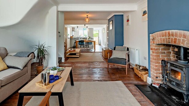 Una sala acogedora con chimenea, un sofá, una mesa de comedor y una cocina al fondo.
