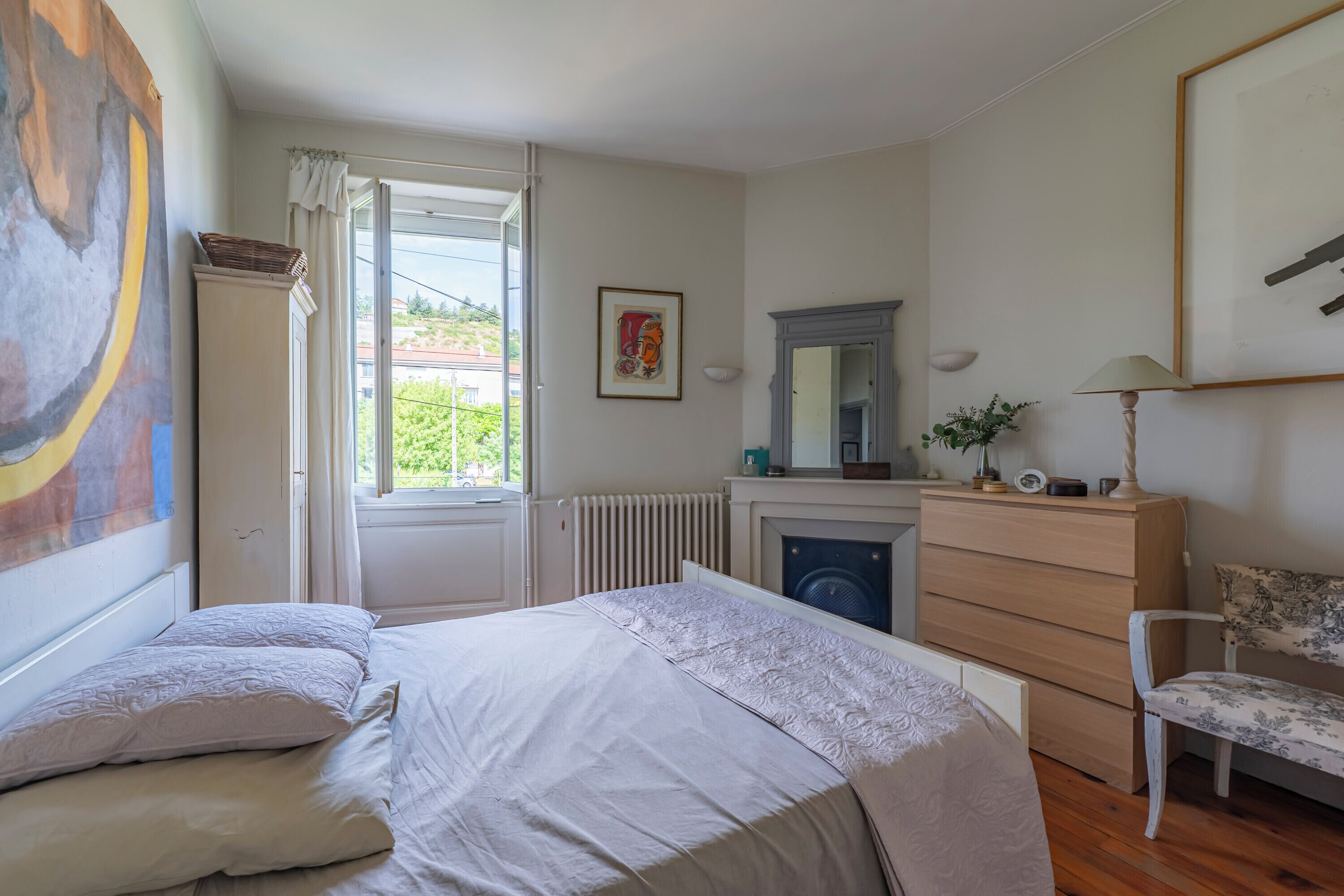 Un dormitorio con cama, cómoda, silla, radiador y ventana con cortinas.