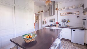 Cocina con armarios blancos, una isla de madera oscura, una campana extractora de acero inoxidable y una variedad de utensilios de cocina en la pared.