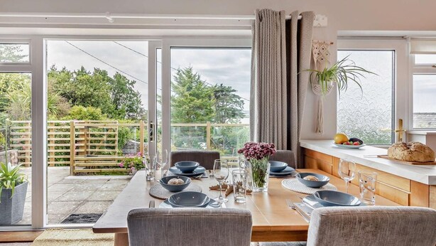 Uma área de refeições com mesa posta para quatro pessoas, grandes janelas e vista para o verde.