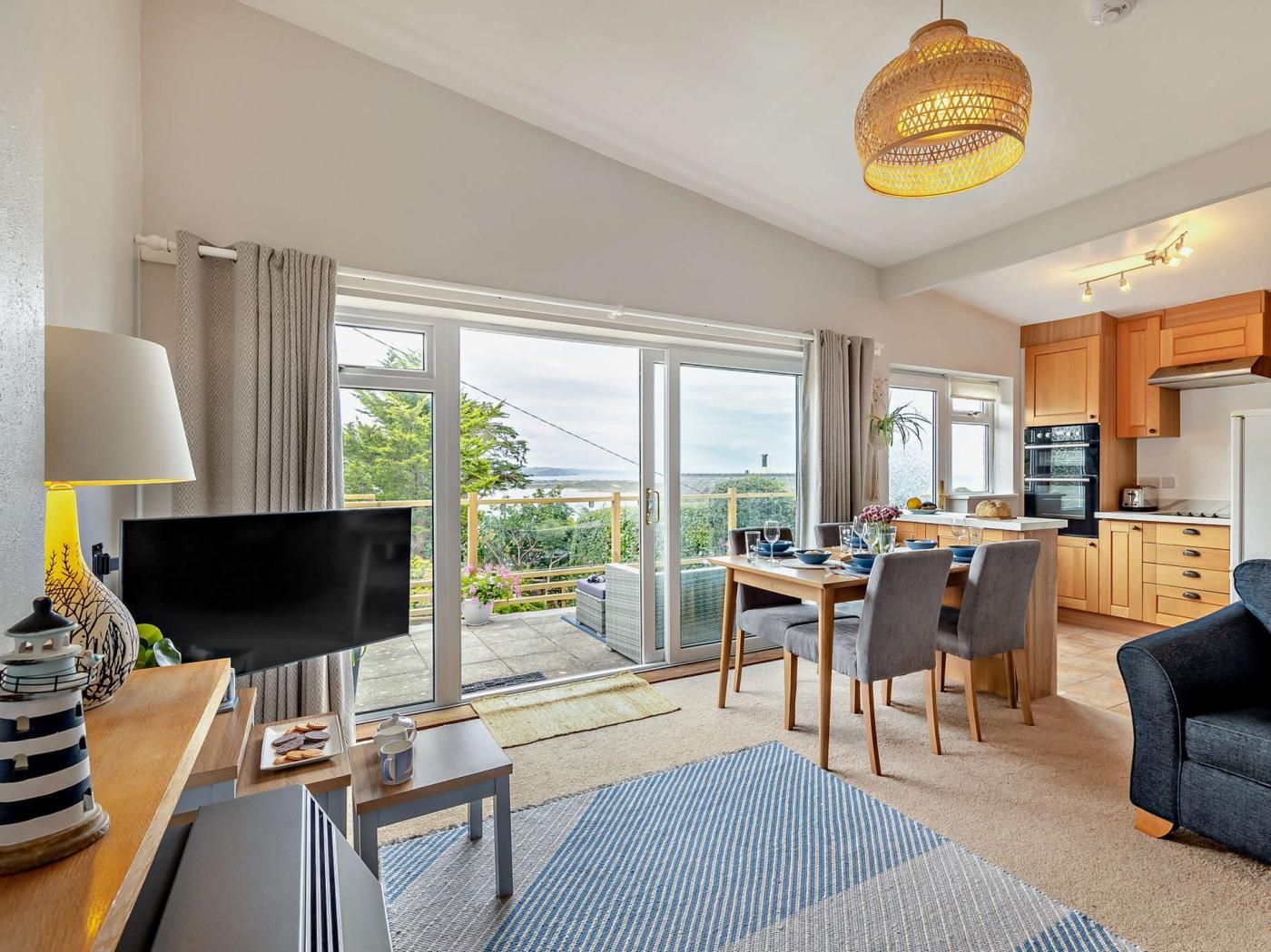 Ein modernes Wohnzimmer mit einem Flachbildfernseher, ein Essbereich mit Tisch und Stühlen, eine Küche mit Holzschränken und ein Balkon mit Aussicht.