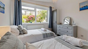 Quarto com duas camas, uma cômoda, um espelho e uma janela com cortinas.