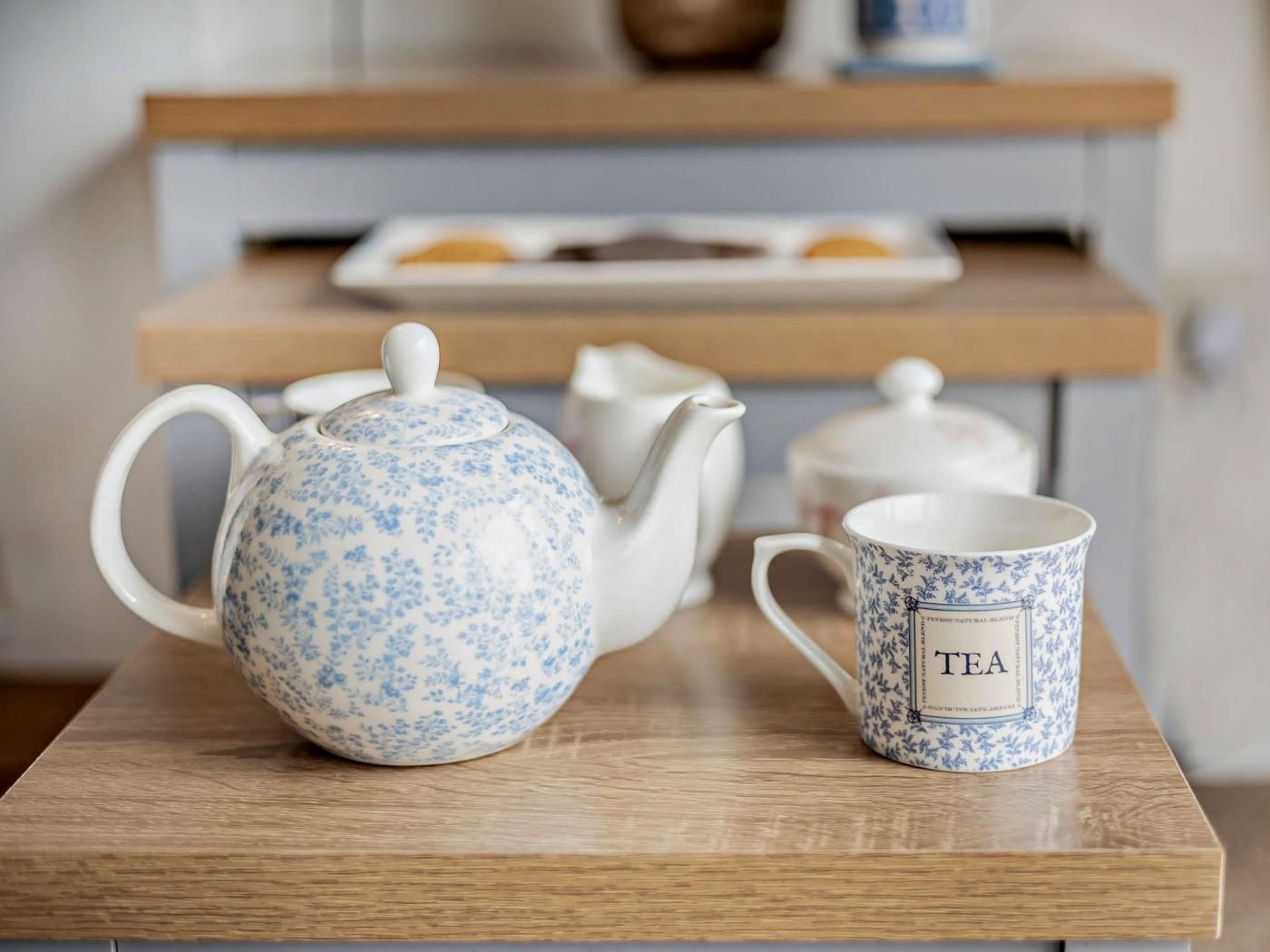 Un service à thé est posé sur une table en bois, avec une tasse sur laquelle est écrit le mot « THÉ » et une théière.