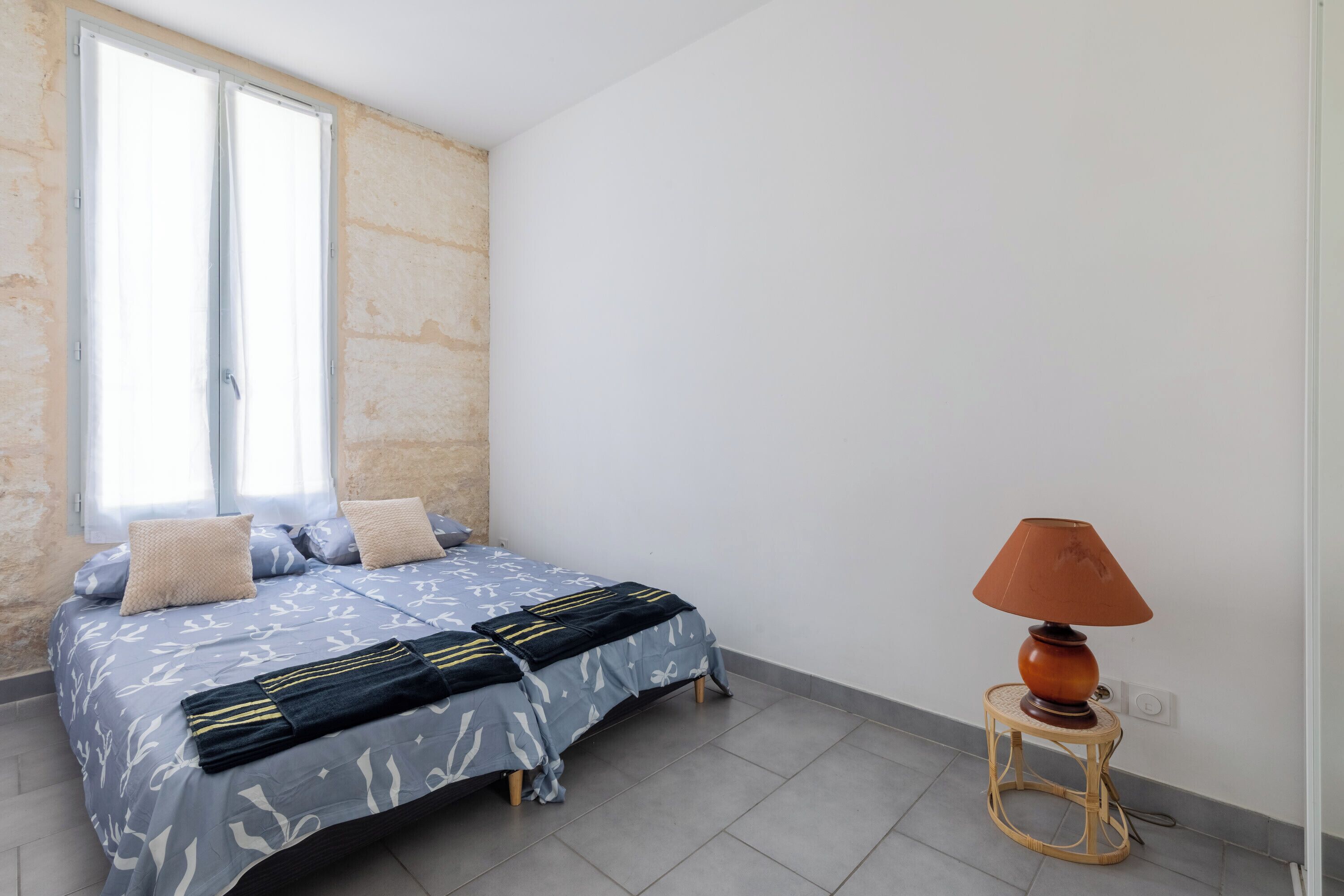 Een slaapkamer met een bed, kussens, een lamp en een raam.
