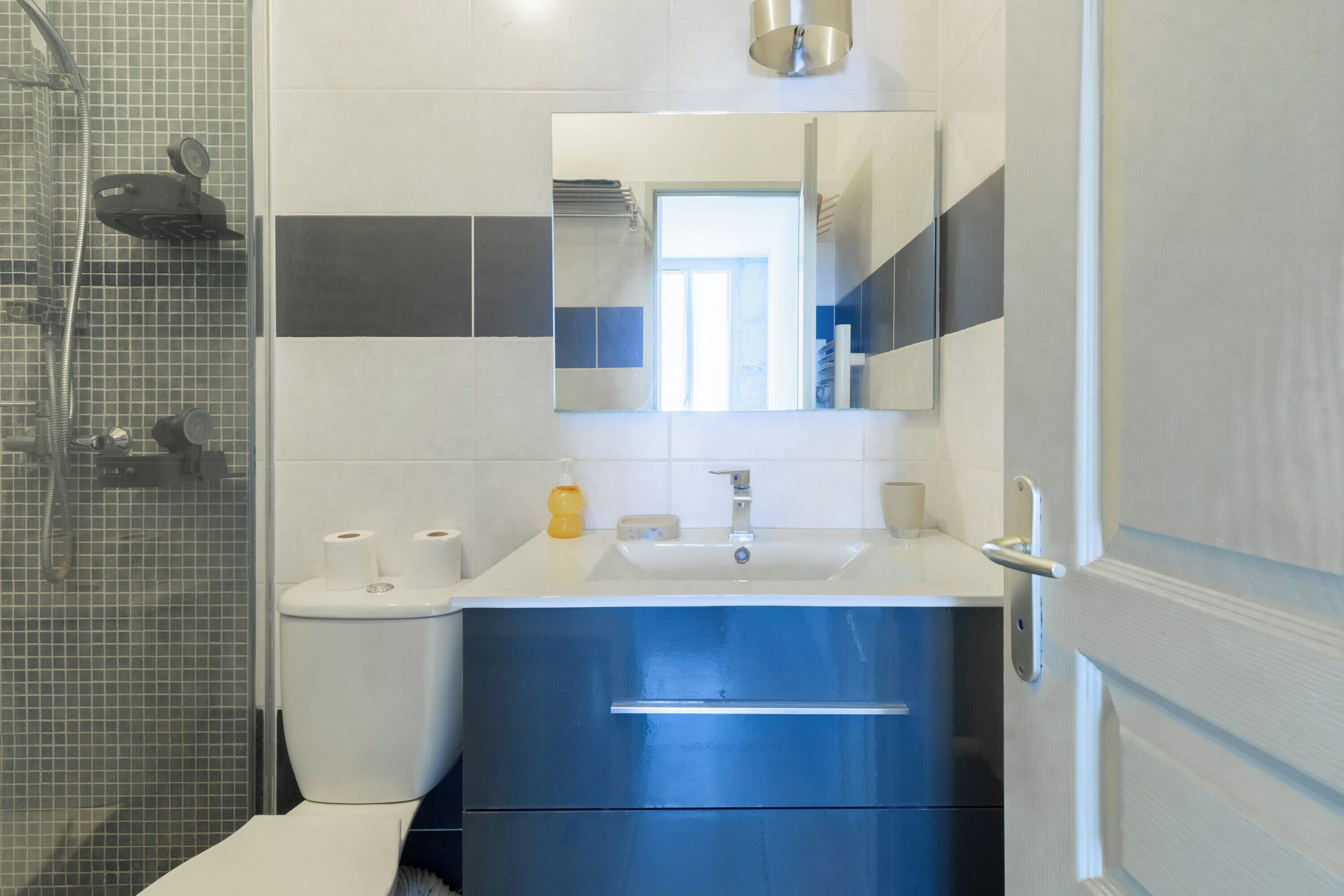 Een badkamer met douche, toilet, wastafel en spiegel.