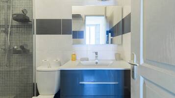 Een badkamer met douche, toilet, wastafel en spiegel.