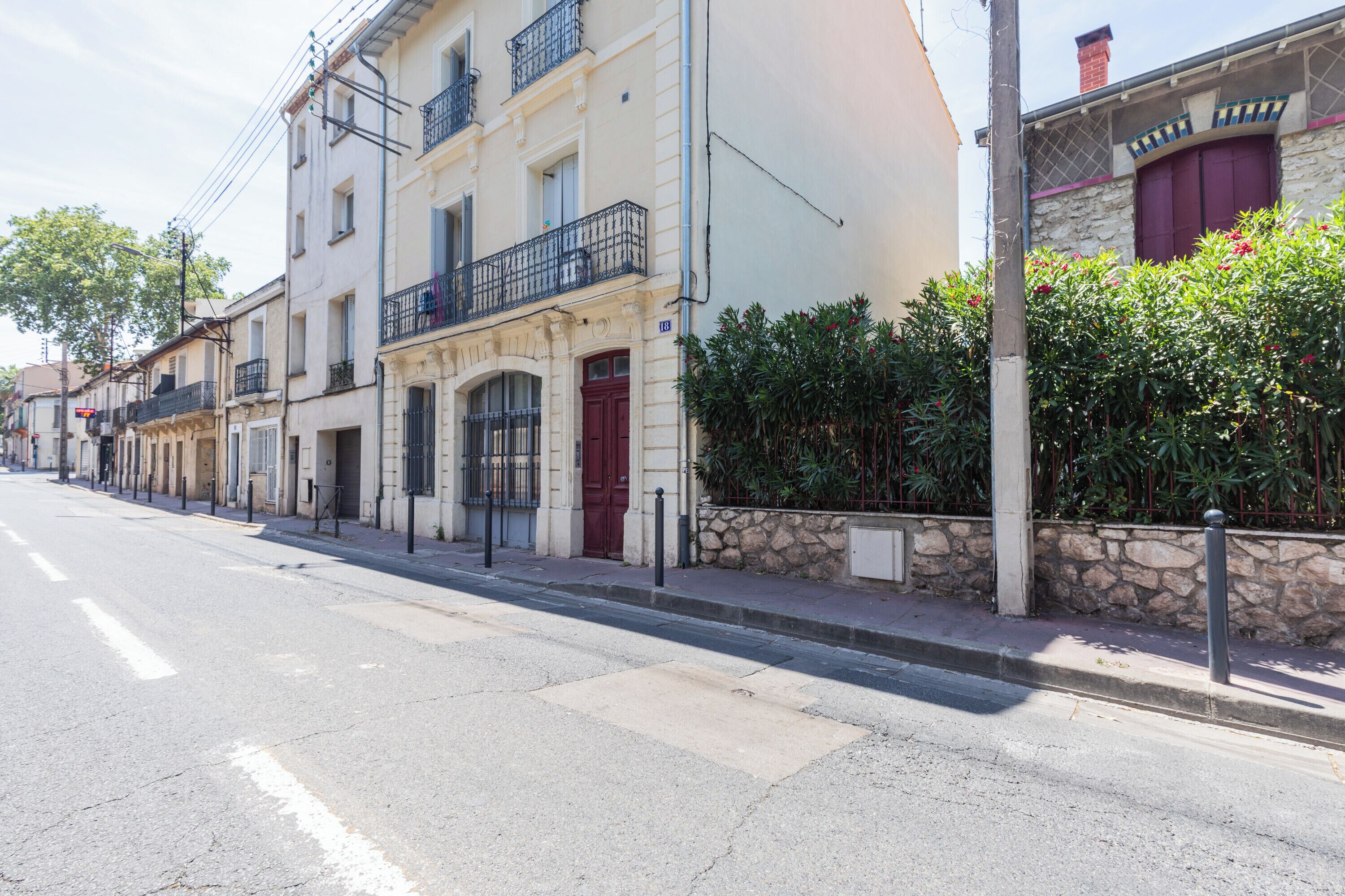 Une rue bordée d’immeubles, avec un trottoir et un ciel dégagé.