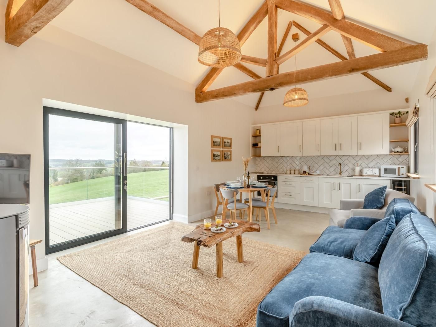 A spacious living area with a large sliding glass door leading to a deck, a kitchen with white cabinets, and a blue sofa.