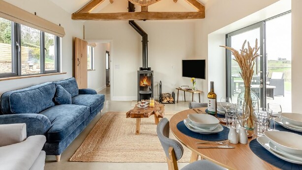 Ein modernes Wohnzimmer mit einer Couch, einem Esstisch für zwei Personen, einem Kamin und großen Fenstern.