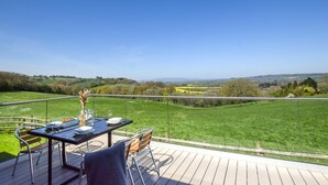 Ein Esstisch draußen mit Blick auf ein grünes Feld und sanfte Hügel in der Ferne.