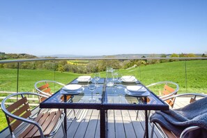Mesa de comedor exterior con sillas, preparada para una comida, con vistas a un paisaje verde.
