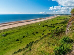A coastal landscape with a beach, grassy fields, and a cliff. - 1 Bed in Forfar (oc-92332) (Burnside)