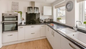Une cuisine moderne dotée d’appareils électroménagers intégrés, de meubles blancs, d’une fenêtre avec stores et d’une horloge murale.