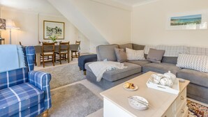 Un salon comprenant un canapé, un fauteuil bleu, une table à manger avec des chaises et un escalier menant à un niveau supérieur.