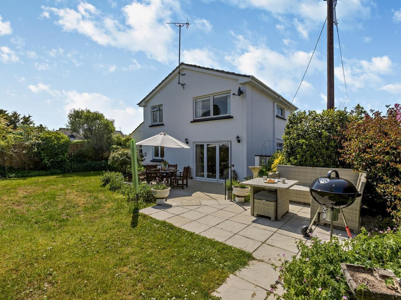 Ein zweistöckiges Haus mit Terrasse, Gartenmöbeln und einem Grill.