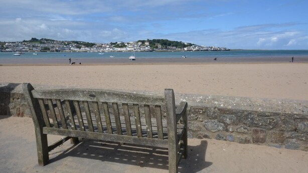 Une plage avec un banc en bois, un mur de pierre et des bateaux sur l’eau.