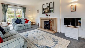 A living room with a sofa, a fireplace, a television, and a large window. - 2 Bed in South Petherton (oc-91952) (South Petherton)