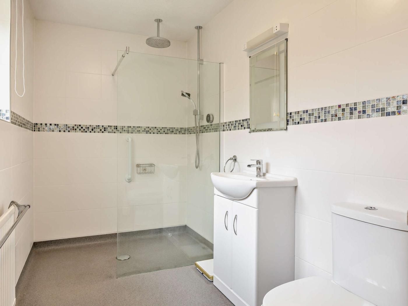 Casa de banho com cabine de duche em vidro, lavatório branco com espelho em cima e sanita.