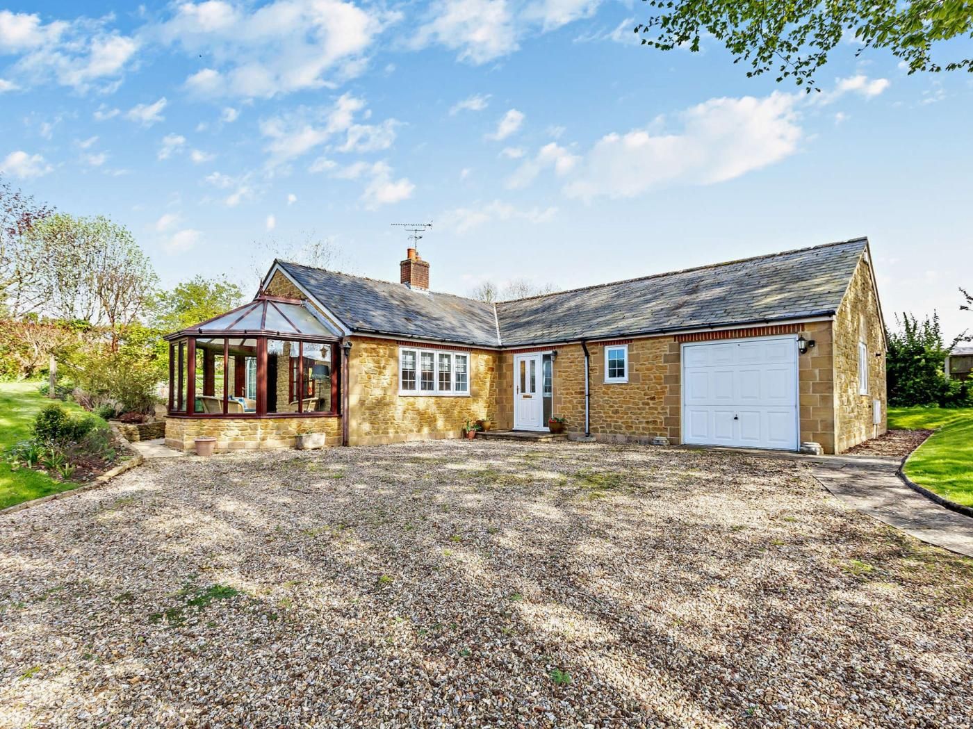 A two-story stone house with a garage, a conservatory, and a gravel driveway.