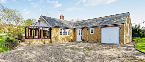 Une maison en pierre à deux étages, dotée d’un garage, d’une véranda et d’une allée gravillonnée.