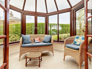 A conservatory with wicker furniture, a small stool, and a view of a garden. - 2 Bed in South Petherton (oc-91952) (South Petherton)