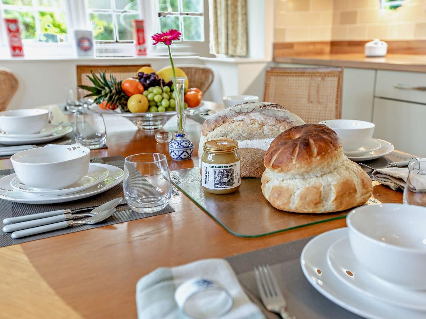 Et morgenbord med brød, en skål med frugt og et syltetøjsglas på et bord.