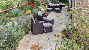 A patio with wicker furniture, a stone floor, and a variety of plants and flowers. - 2 Bed in South Petherton (oc-91952) (South Petherton)