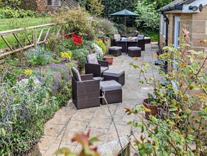 Eine Terrasse mit Korbmöbeln, Steinboden und verschiedenen Pflanzen und Blumen.