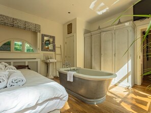 Ein Schlafzimmer mit einem großen Bett, einer Fußgängerbadewanne, einem Schminktisch mit Spiegel und einem Kleiderschrank.