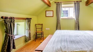 Ein Zimmer mit einem Bett, einem Sessel, einem Fenster mit Vorhängen und einer hölzernen Bank.