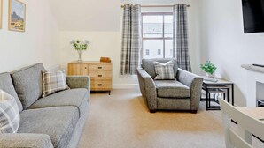 Ein Wohnzimmer mit Sofa, Sessel, Holzkommode und Fernseher.