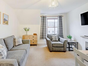 A living room with a sofa, armchair, wooden dresser, and a TV. - 2 Bed in Keswick (oc-91901) (Keswick)