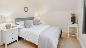 Ein Schlafzimmer mit einem Bett, Nachttischen, einem Fernseher auf einem Schrank, einer Wandleuchte und einer Deckenlampe.