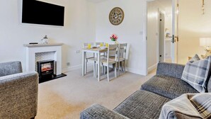 Ein Wohnzimmer mit Kamin, einem Esstisch mit Stühlen, einem flachbildfernseher über dem Kamin und einer Wanduhr.