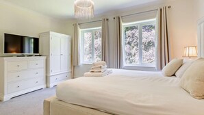 Un dormitorio con cama, televisión, armario y ventana con cortinas.