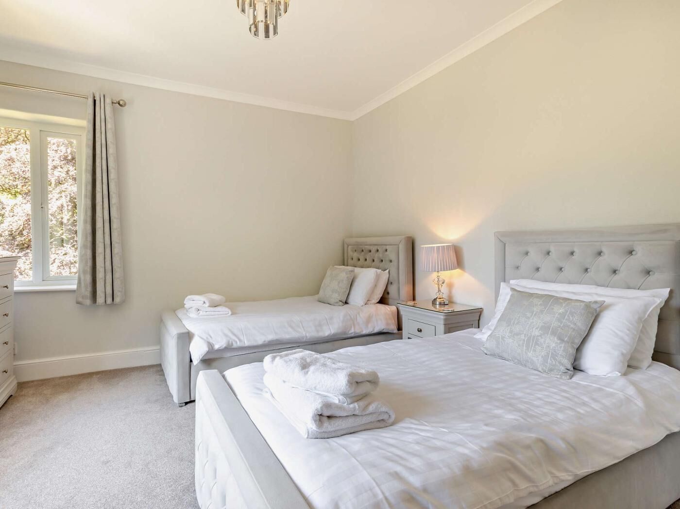 A bedroom with two beds, a nightstand with a lamp, and a window with curtains.