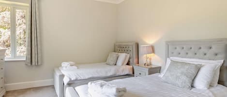 A bedroom with two beds, a nightstand with a lamp, and a window with curtains.