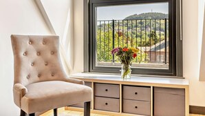 Ein Zimmer mit Fenster, einem Sessel, einer Vase mit Blumen und einer Holzbänkschrank.