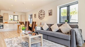 Ein modernes Wohnzimmer mit grauem Sofa, einem Couchtisch und einem Essbereich mit Stühlen und Tisch.