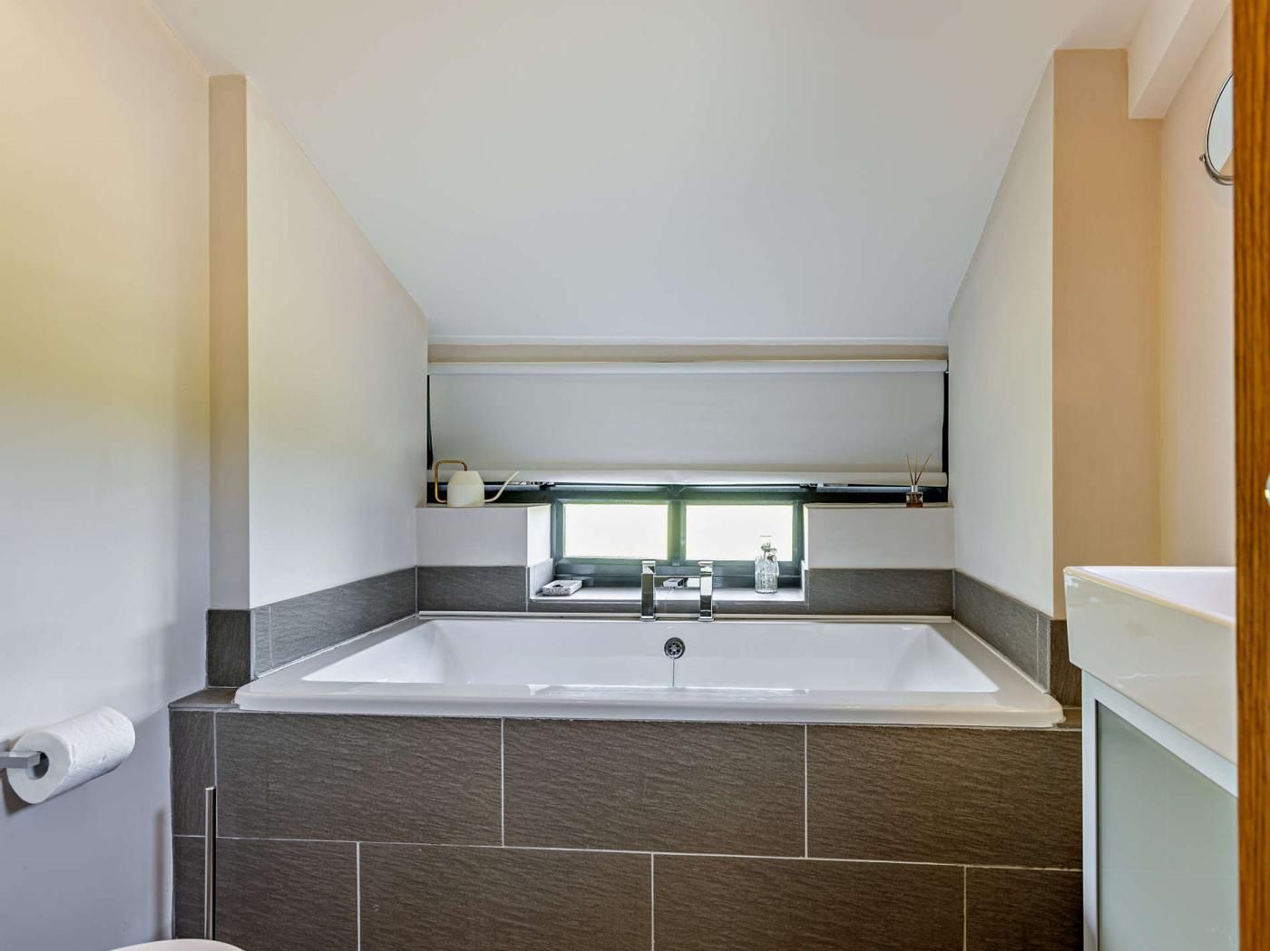 A bathroom with a bathtub, a window above the sink, and a toilet.