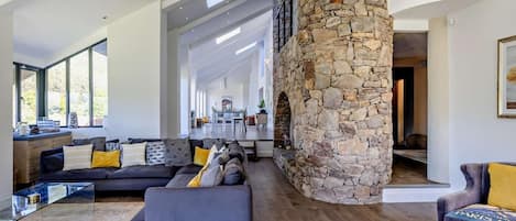 Un salon moderne avec une colonne en pierre, un ensemble de canapés, une table basse en verre et une vue sur l’extérieur.