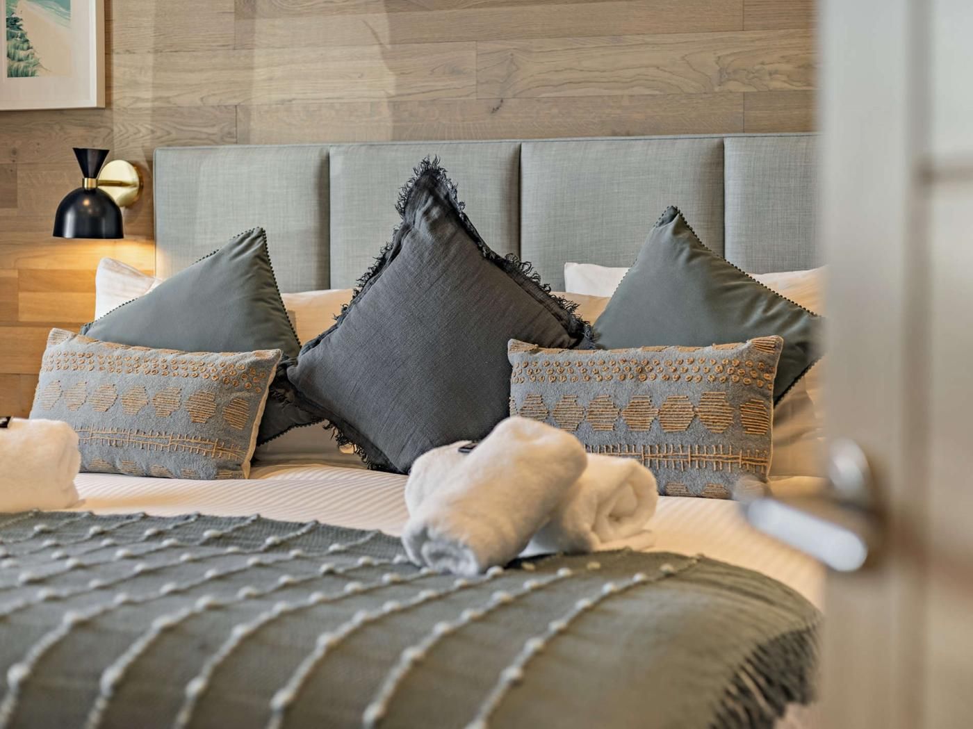 A neatly made bed with a grey headboard, multiple pillows, and a blanket.