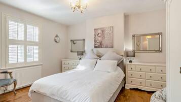 A bedroom with a bed, bedside tables, a chandelier, a window with blinds, and a wall clock.