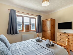 Quarto com cama, guarda-roupa de madeira, televisão e janela com cortinas.