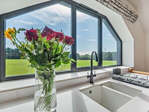 Eine Küche mit großem Fenster, Blumen in einer Vase und einem modernen Wasserhahn.