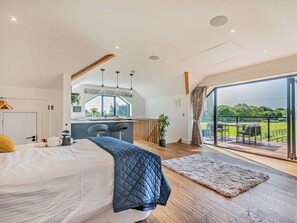 Ein modernes Schlafzimmer mit einem großen Bett, einem Schreibtisch, Blick ins Freie und einem Balkon.
