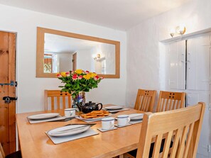 A dining area with a wooden table set for two, a vase of flowers, and a mirror above the table. - 2 Bed in Braunton (oc-92387) (Croyde)