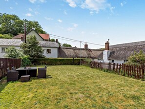 A backyard with a dining area, a thatched-roof house, and a wooden fence. - 2 Bed in Braunton (oc-92387) (Croyde)