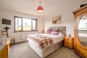 A bedroom with a bed, a window, a TV, a wooden dresser, and a mirror. - 3 Bed in Grange-over-sands (oc-92389) (Upper Allithwaite)