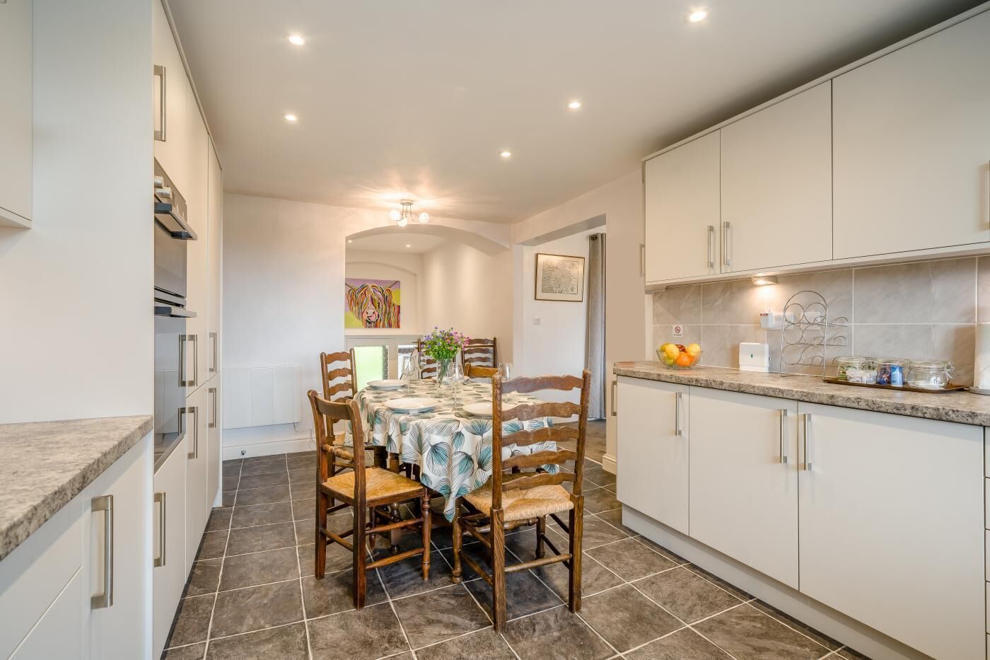 A modern kitchen with white cabinets, a dining table set for four, and a tiled floor.